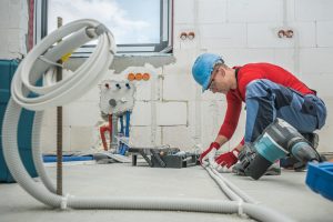 Caucasian Professional Electrician at Work. Electric Cables Plastic Pipe Conduit Installation Inside Newly Constructed House.