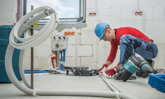 Caucasian Professional Electrician at Work. Electric Cables Plastic Pipe Conduit Installation Inside Newly Constructed House.